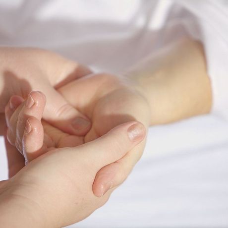 Hands gently holding a wrist in a soft, white bed setting