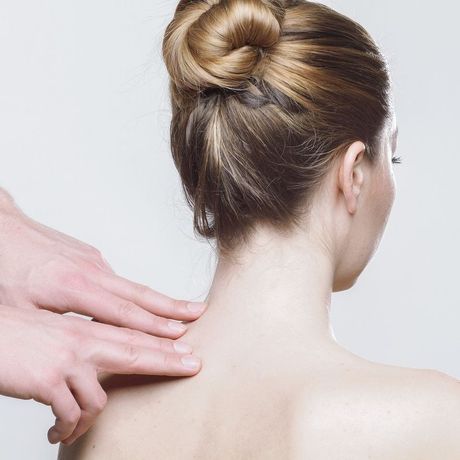 Hands massaging a woman's neck and shoulders from behind, with hair in a bun.
