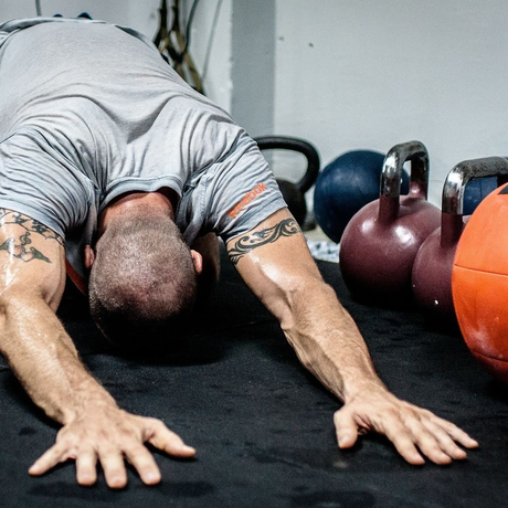Person stretching in a yoga pose on a gym floor beside medicine balls