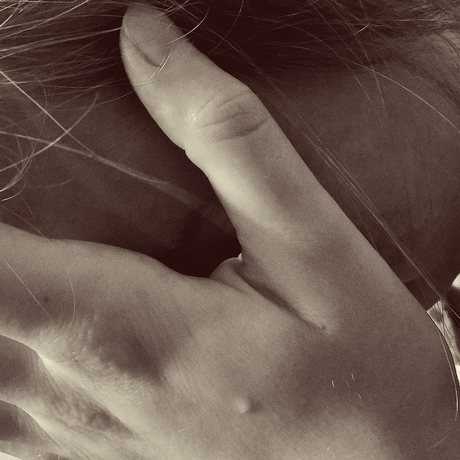 Hand covering part of a face, with strands of hair across a sepia-toned close-up.