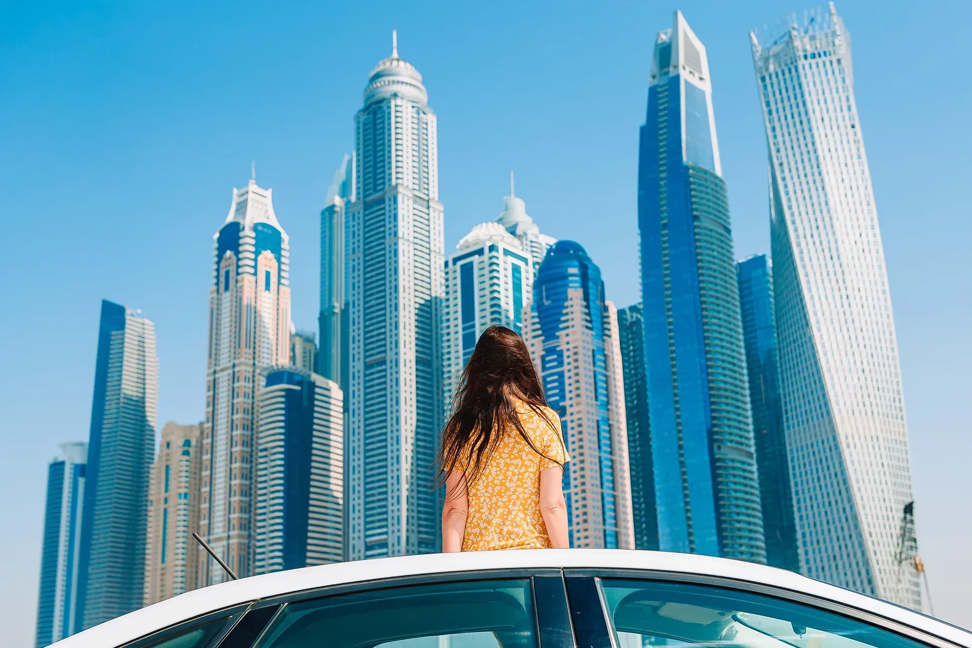 woman sat on top of a car looking towards towers in Dubai Marina