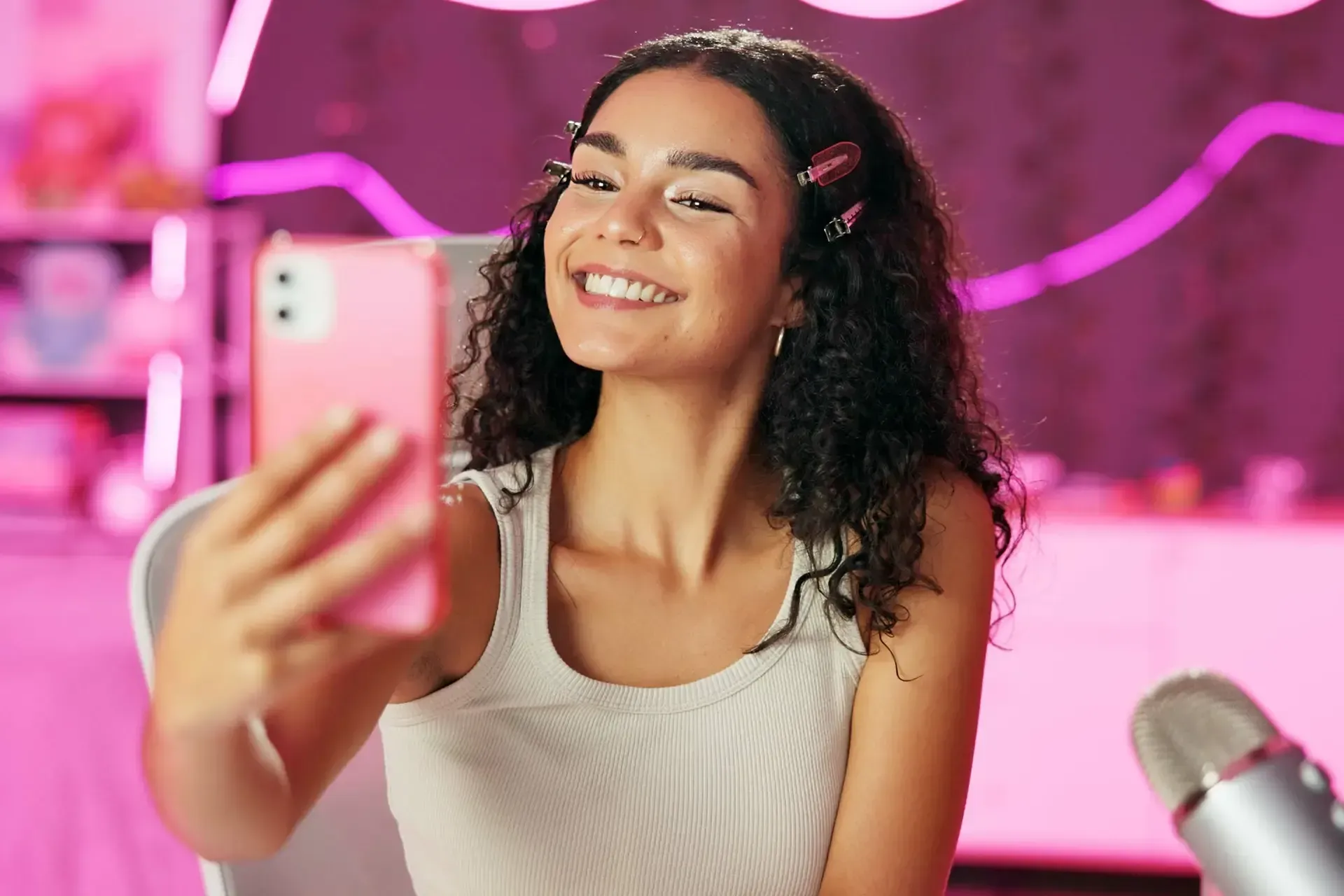 A woman is recording herself with her cell phone in front of a ring light.