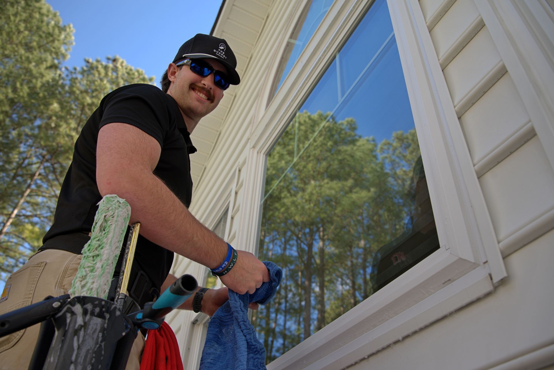 Man cleaning a large window with a squeegee and microfiber cloth; outdoors, sunny.