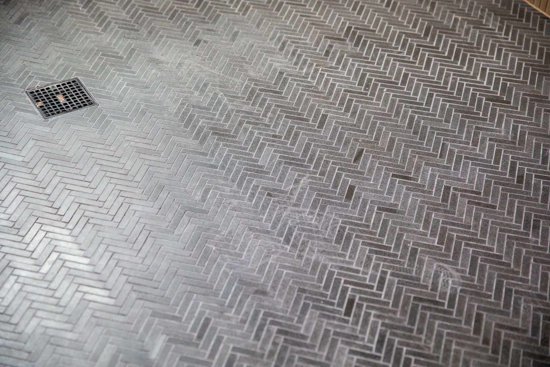 A close up of a herringbone tile floor with a drain.
