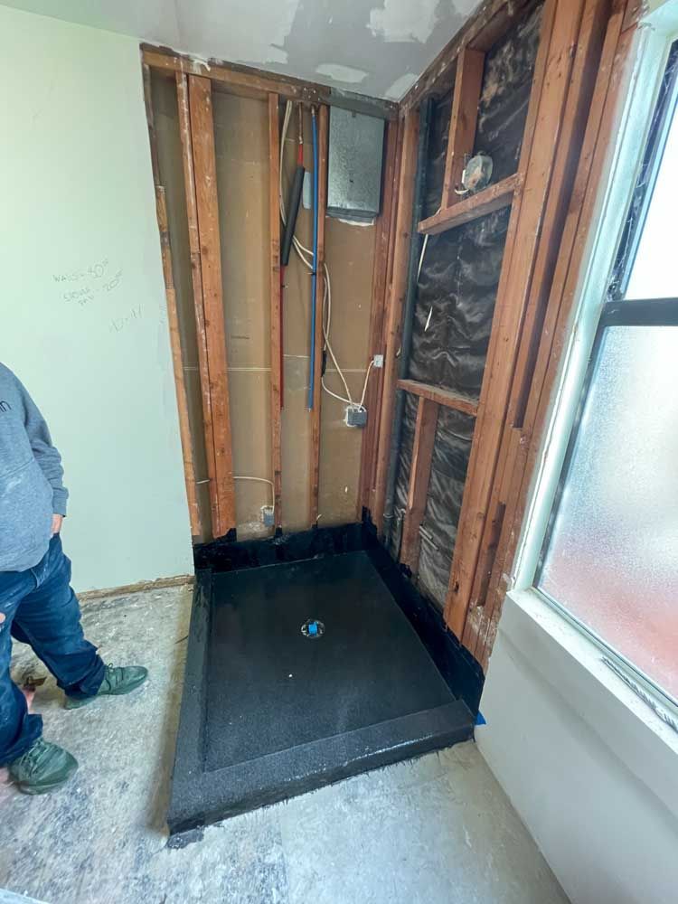 A man is standing in a room with a shower stall in it.