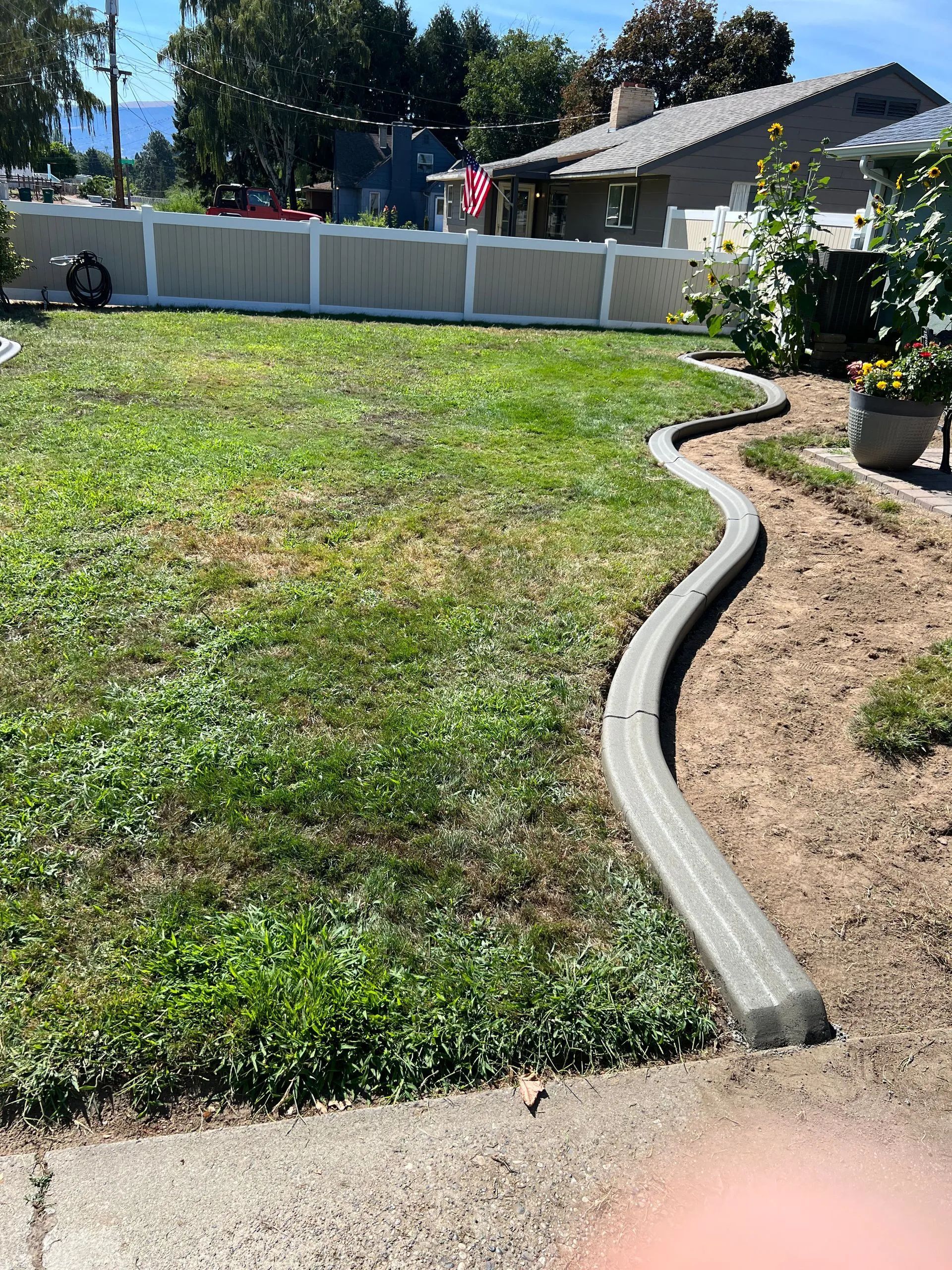 Lawn with a concrete border, grass, and a white fence in a backyard setting.