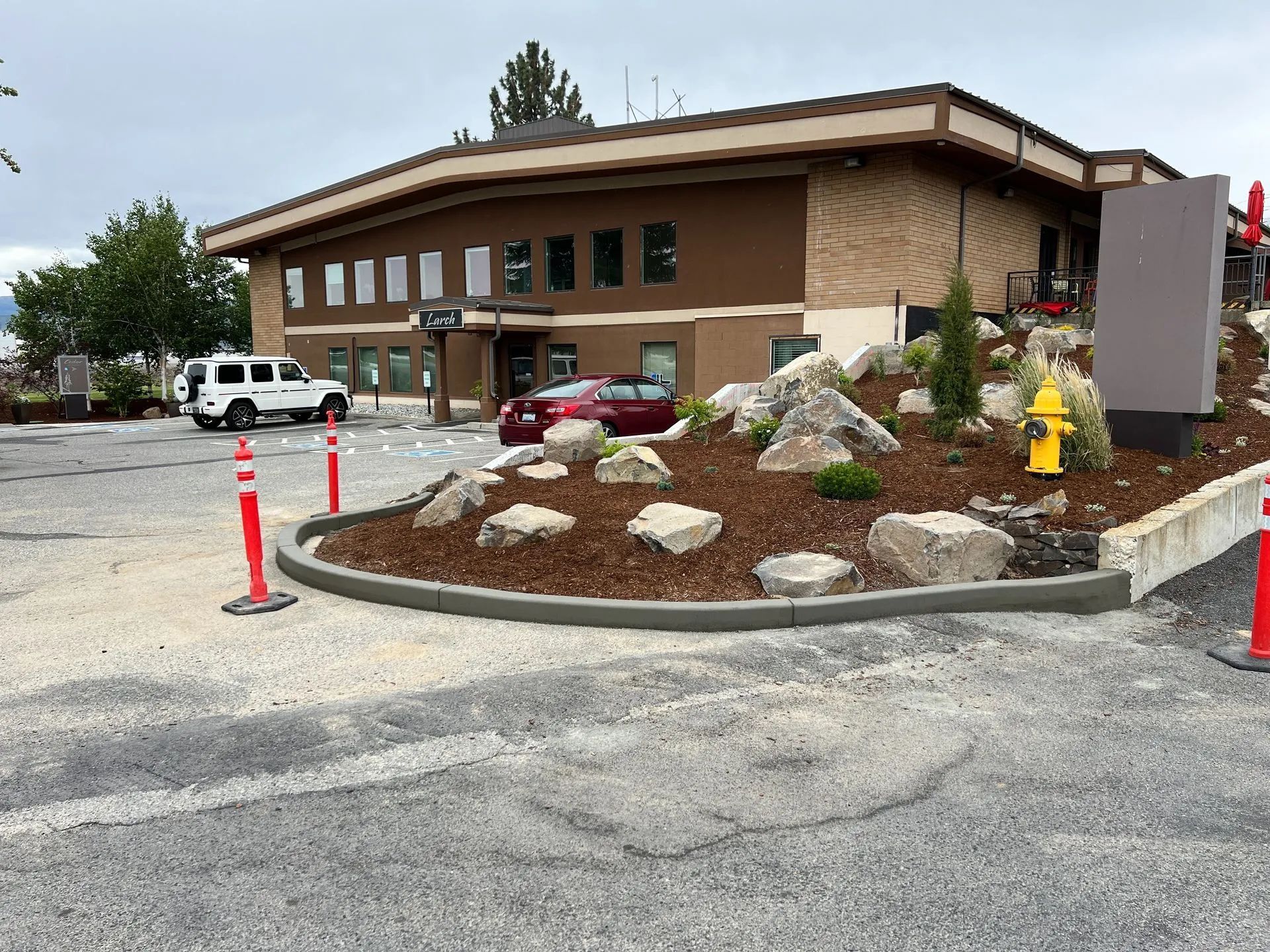 Building exterior with a red car and white SUV parked in front. Landscaping includes rocks and mulch.