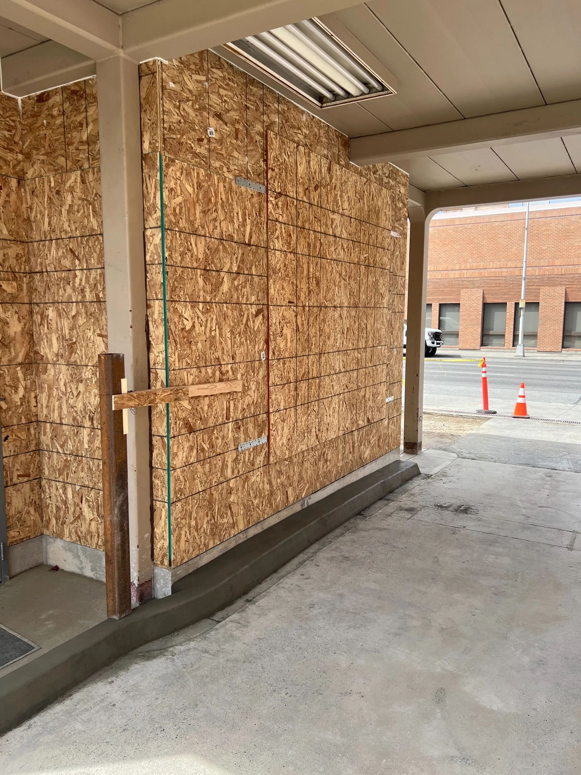 Construction site: OSB-sheathed wall with concrete floor and curb; metal roof; street in background.