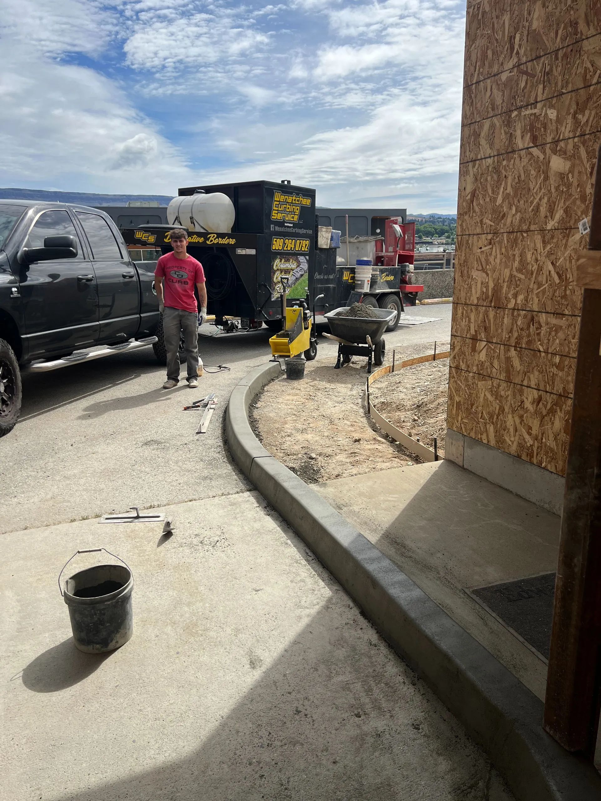 Construction site with a truck, workers, and a freshly poured concrete curb.