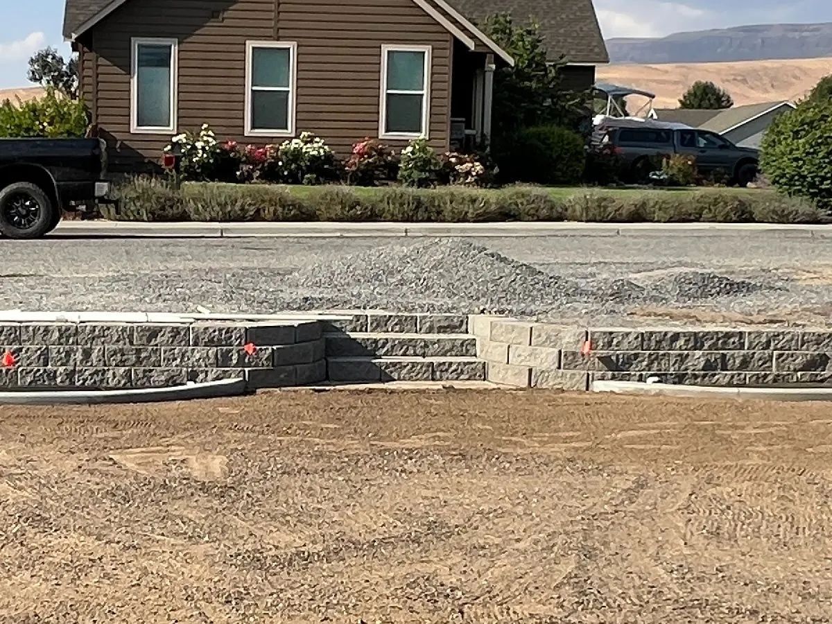 Construction site: Retaining wall with steps leading up to a gravel driveway. A house is in the background.
