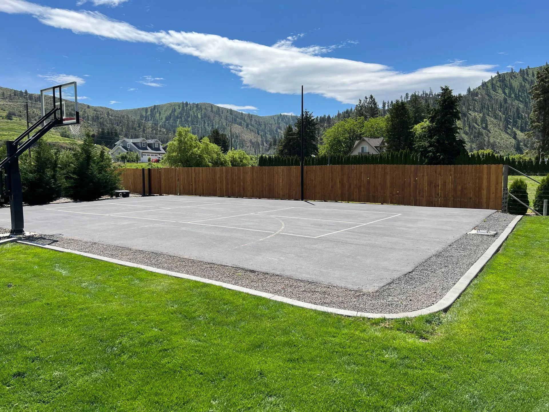 Basketball court in a backyard with a fence and mountain backdrop.