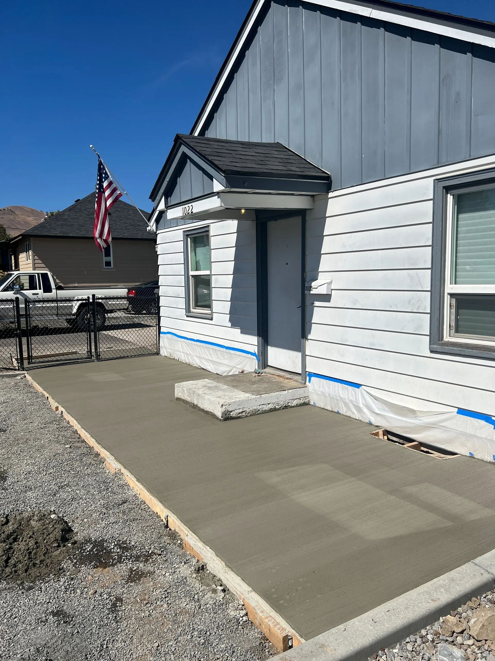 Newly poured concrete patio next to a house with blue siding and a covered doorway.