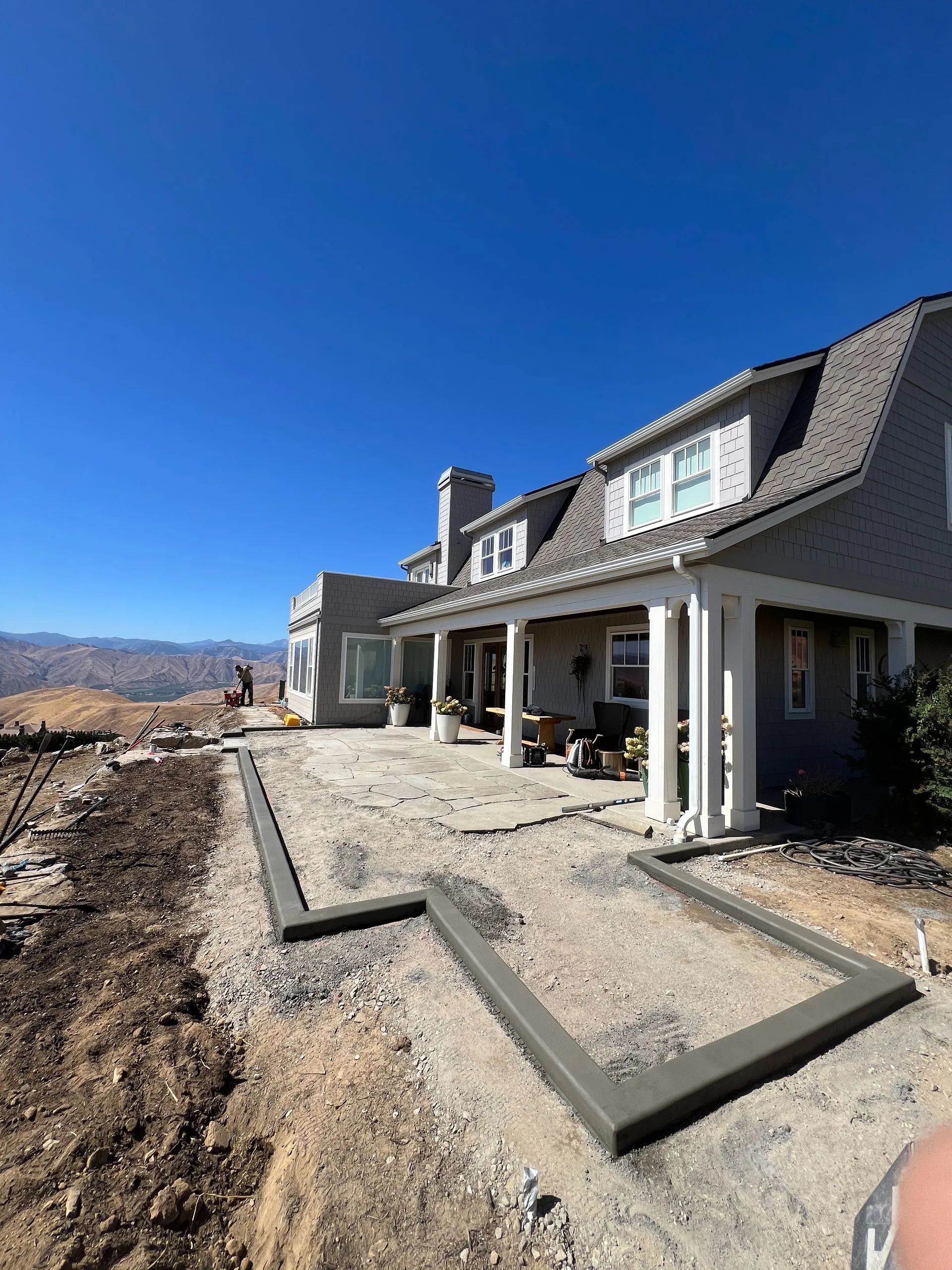 Concrete patio construction near a light grey house with a blue sky background.