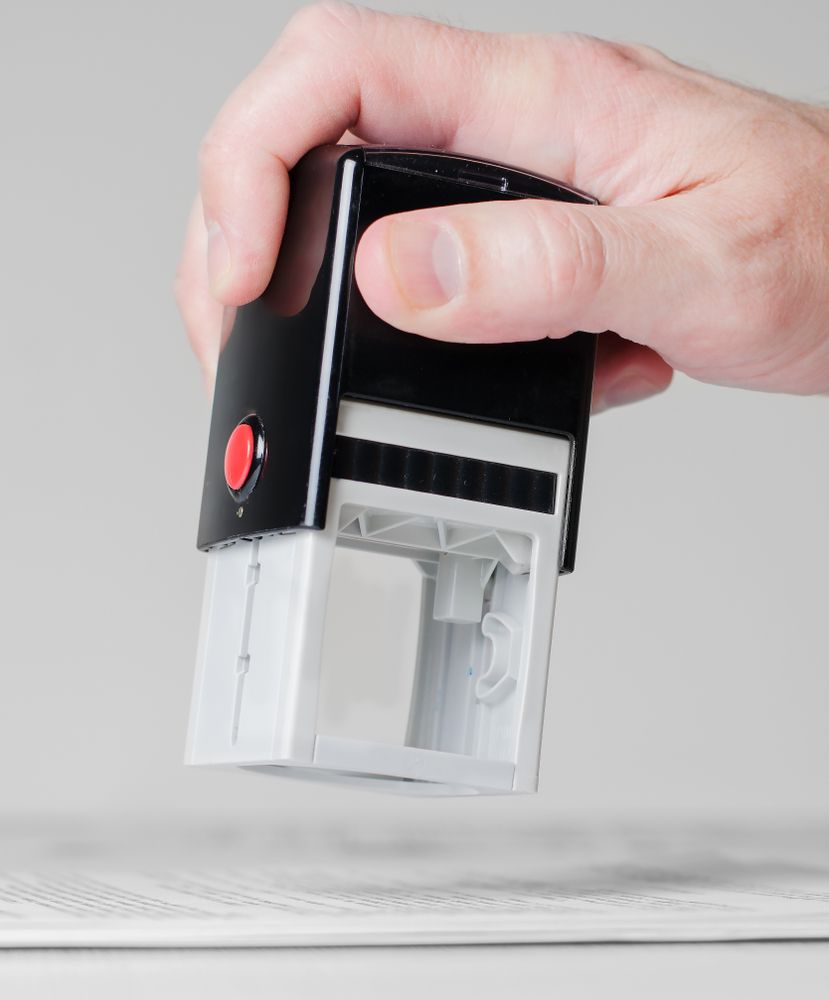 A person is holding a black and white stamp with a red button