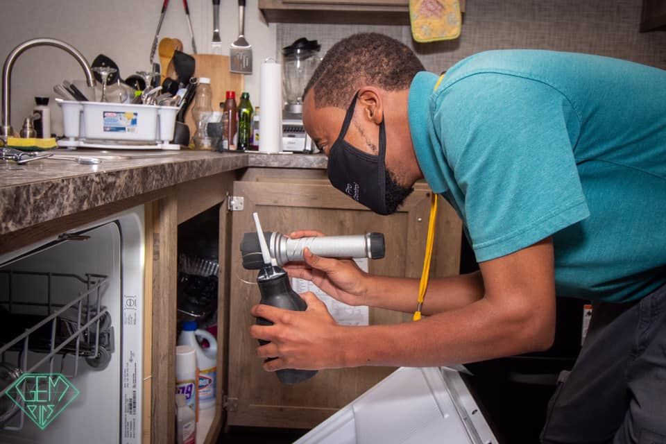 A man wearing a mask is working on a sink in a kitchen.