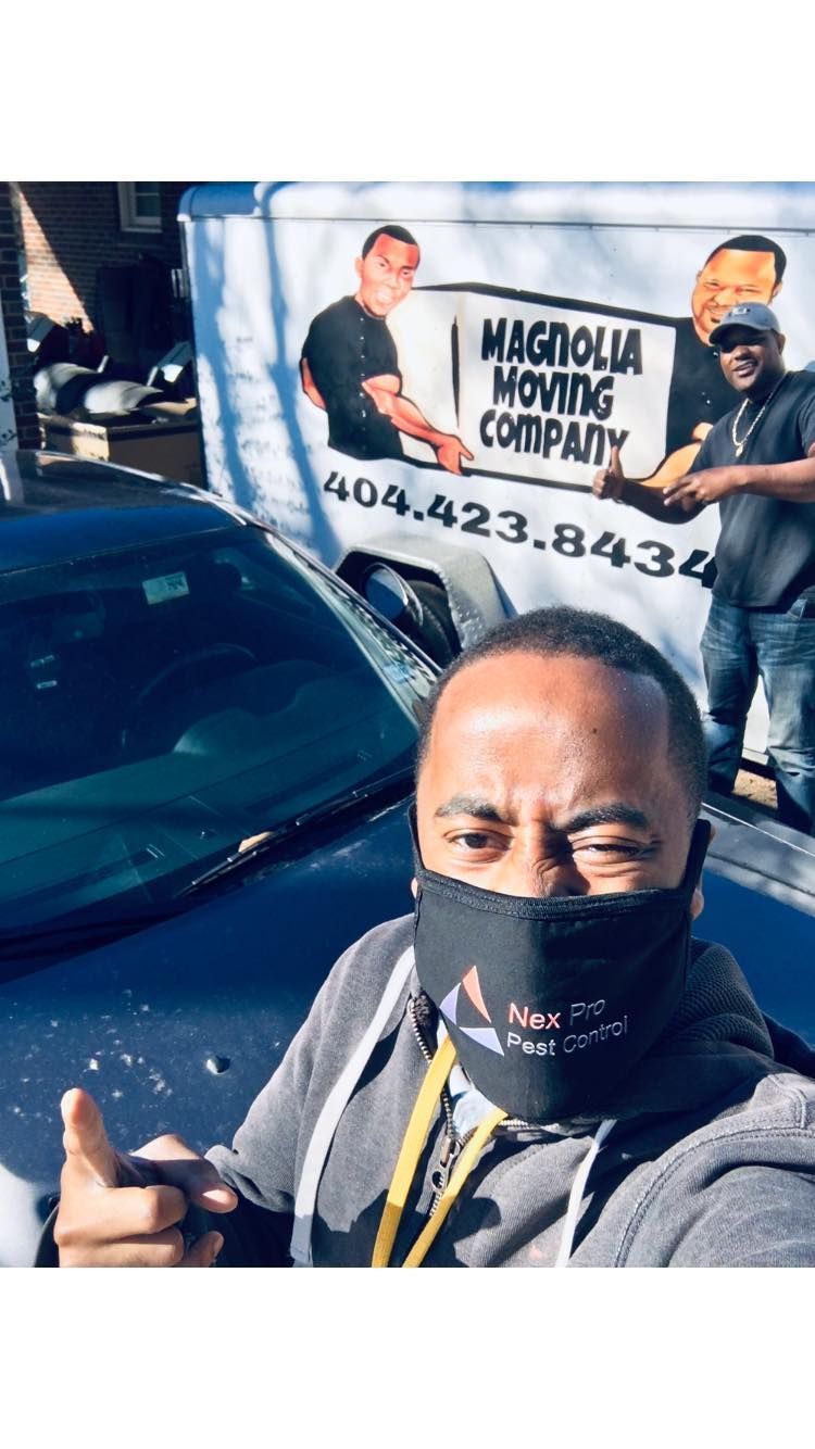 A man wearing a mask is standing in front of a moving company truck.