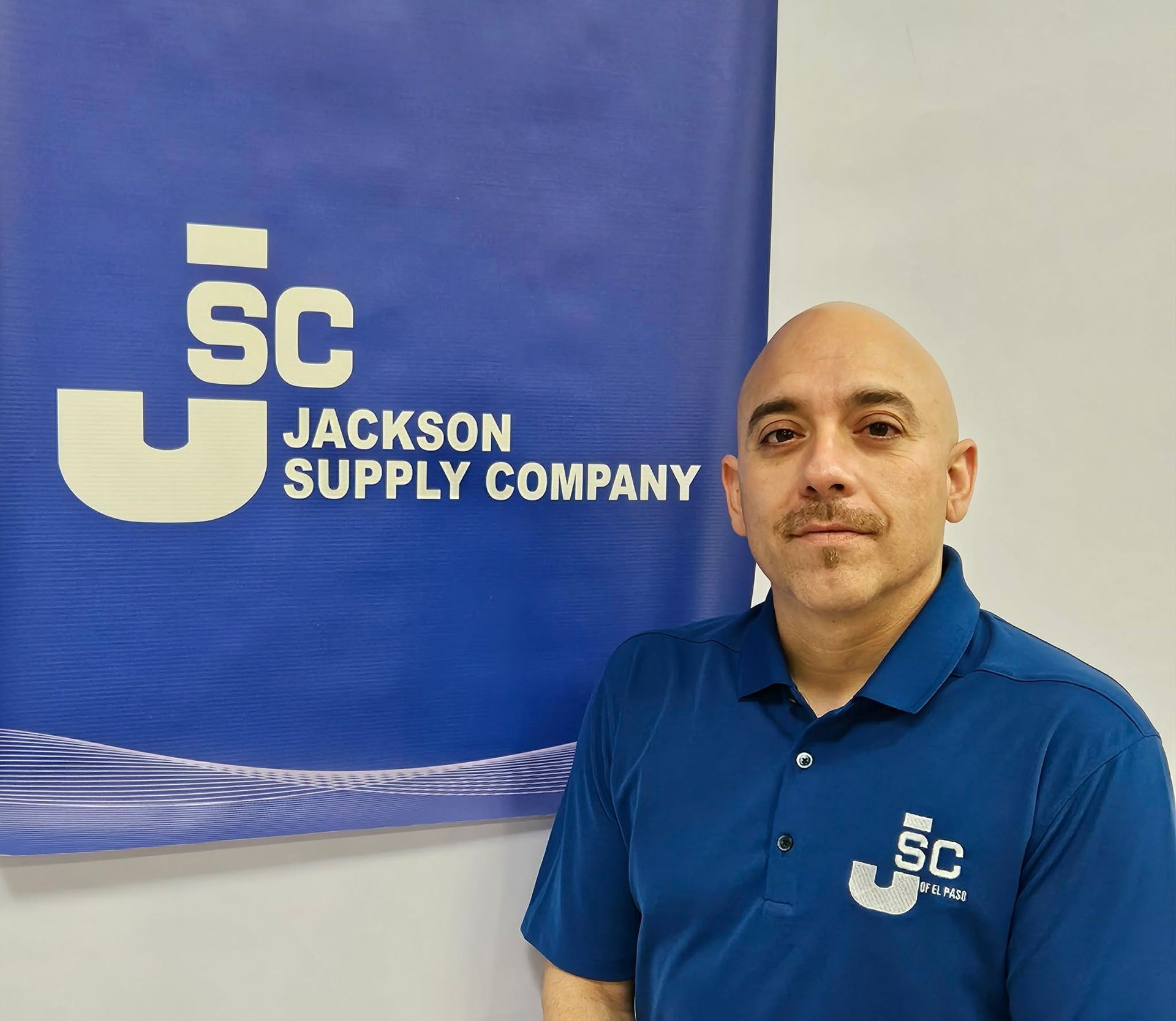 A person standing in front of a blue Jackson Supply Company banner, wearing a blue polo shirt with the company logo.