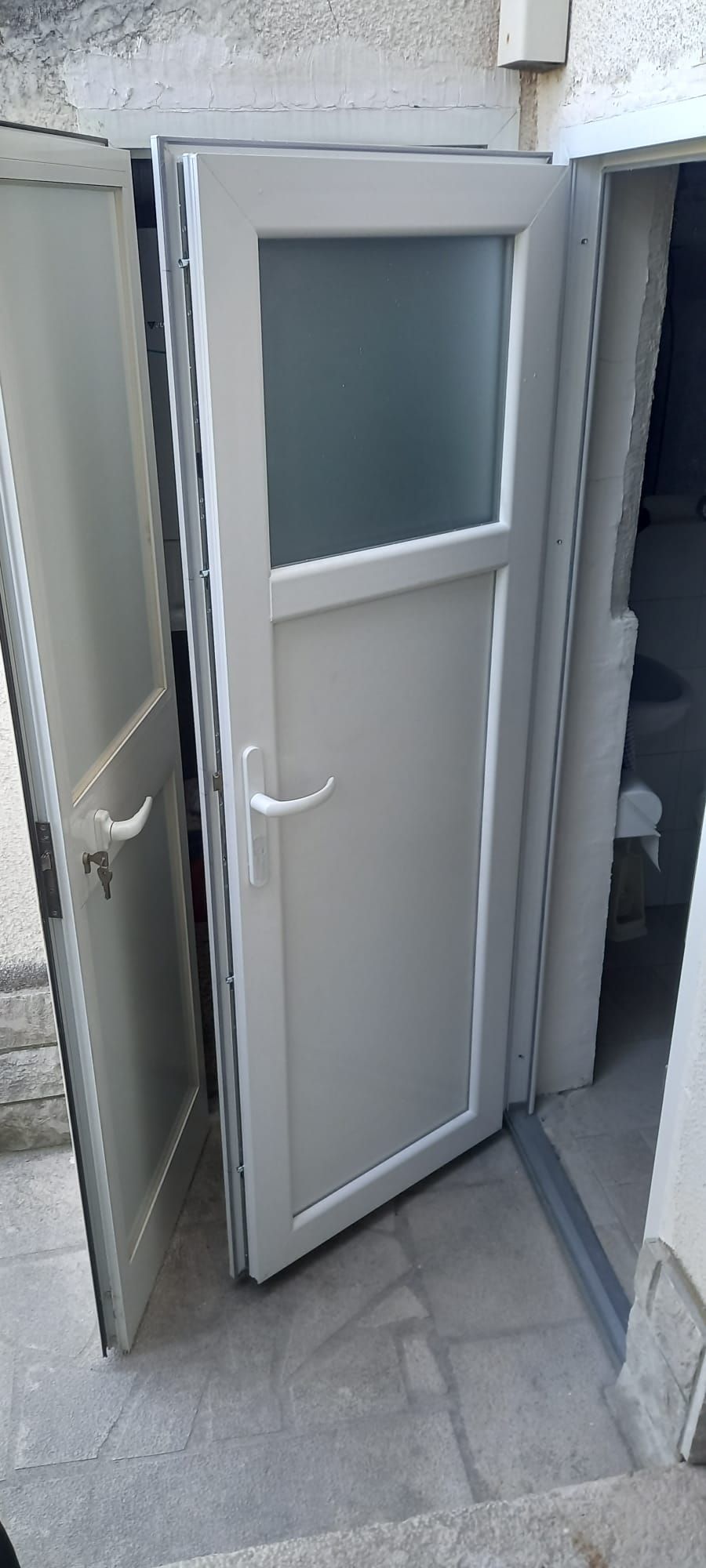 Apri una porta bianca con pannello in vetro satinato che conduce a uno stretto ingresso piastrellato.