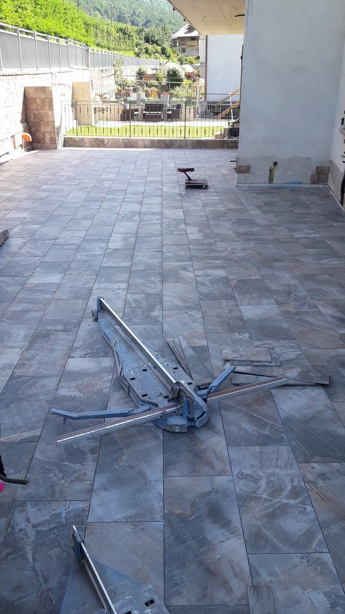 Un patio piastrellato con pezzi di metallo sparsi e un piccolo gatto nero in lontananza.