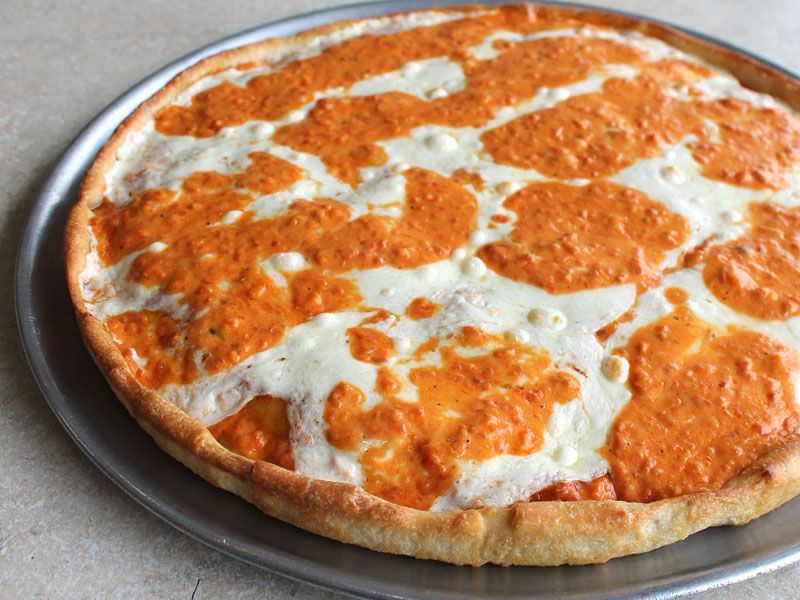 Pizza with creamy white cheese and orange sauce on a metal pan.