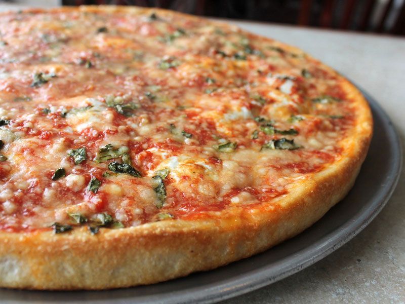 Pizza on a metal tray, with red sauce, cheese, and basil, close up.