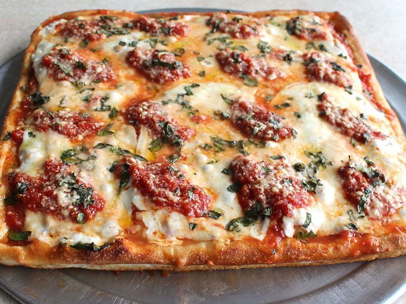 Square pizza with tomato sauce, mozzarella, and basil on a metal tray.