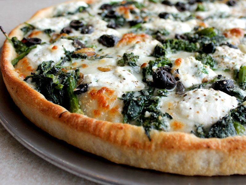 Pizza with spinach, ricotta cheese, and olives on a gray plate.