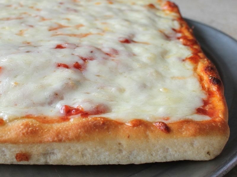 Square cheese pizza on a gray plate; baked dough with melted white cheese and red sauce.