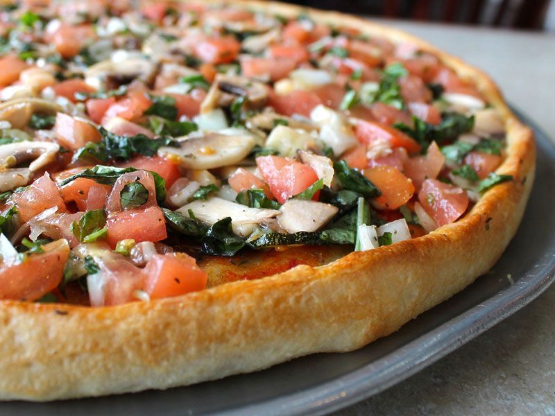 Deep-dish pizza topped with diced tomatoes, mushrooms, basil, and onions on a gray plate.