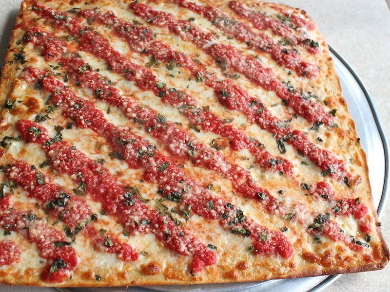 Square pizza with diagonal tomato sauce stripes and basil on a metal tray.