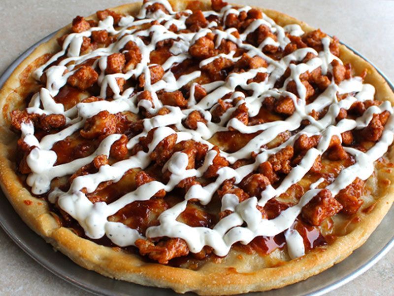 Pizza with chicken, barbecue sauce, and white drizzle on a metal pan.