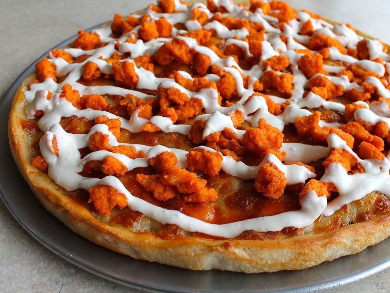 Buffalo chicken pizza with orange chicken pieces and white drizzle on a crust.