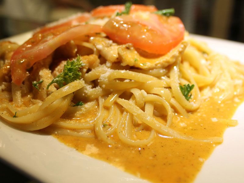 Linguine pasta in creamy orange sauce, topped with sliced tomatoes, cheese, and parsley.