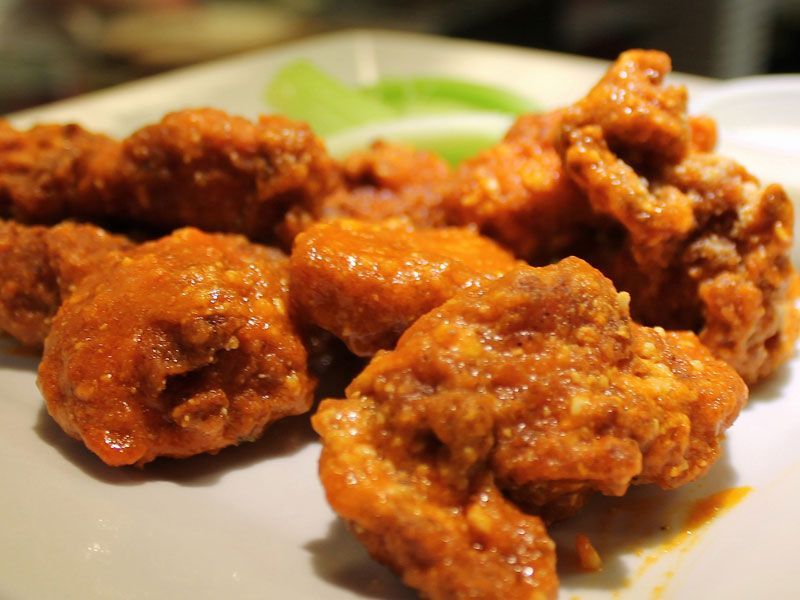 Buffalo wings coated in orange sauce on a white plate, with celery sticks in the background.
