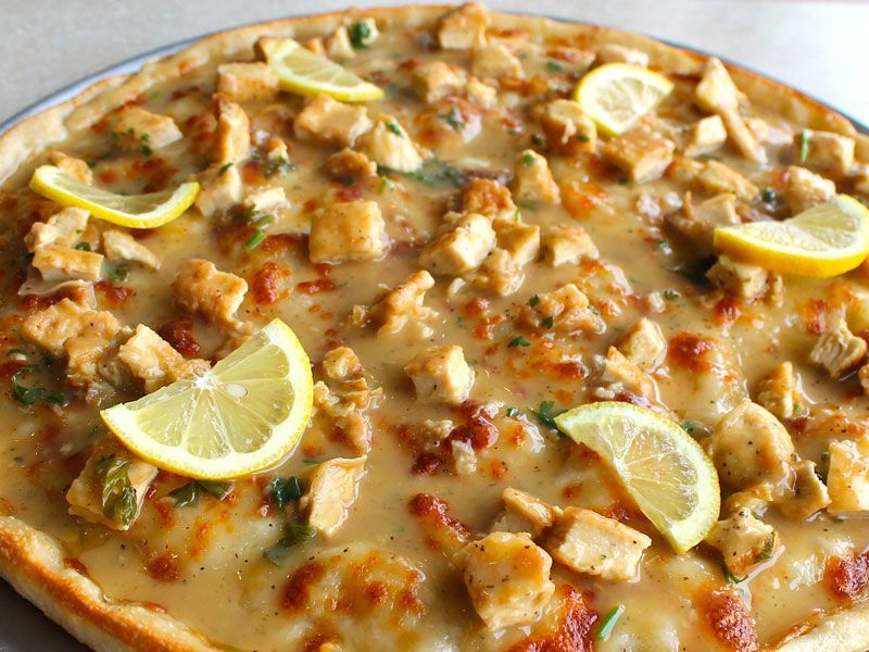 Pizza topped with chicken, sauce, cheese, and lemon slices.