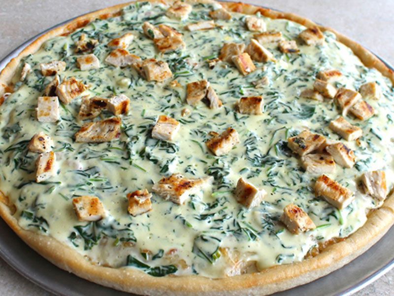 Chicken and spinach pizza with creamy white sauce on a silver pan.
