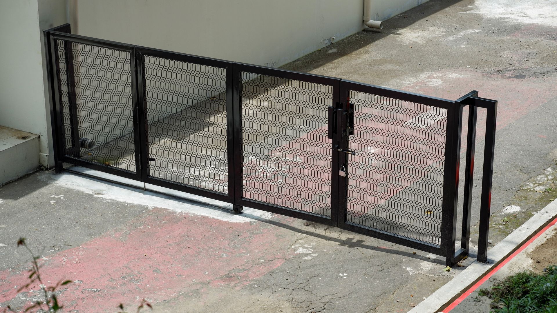 Black metal mesh gate blocking a concrete ramp beside a building wall