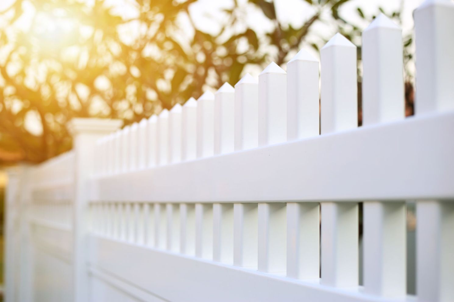 White wooden fence with warm sunlight and blurred trees in the background