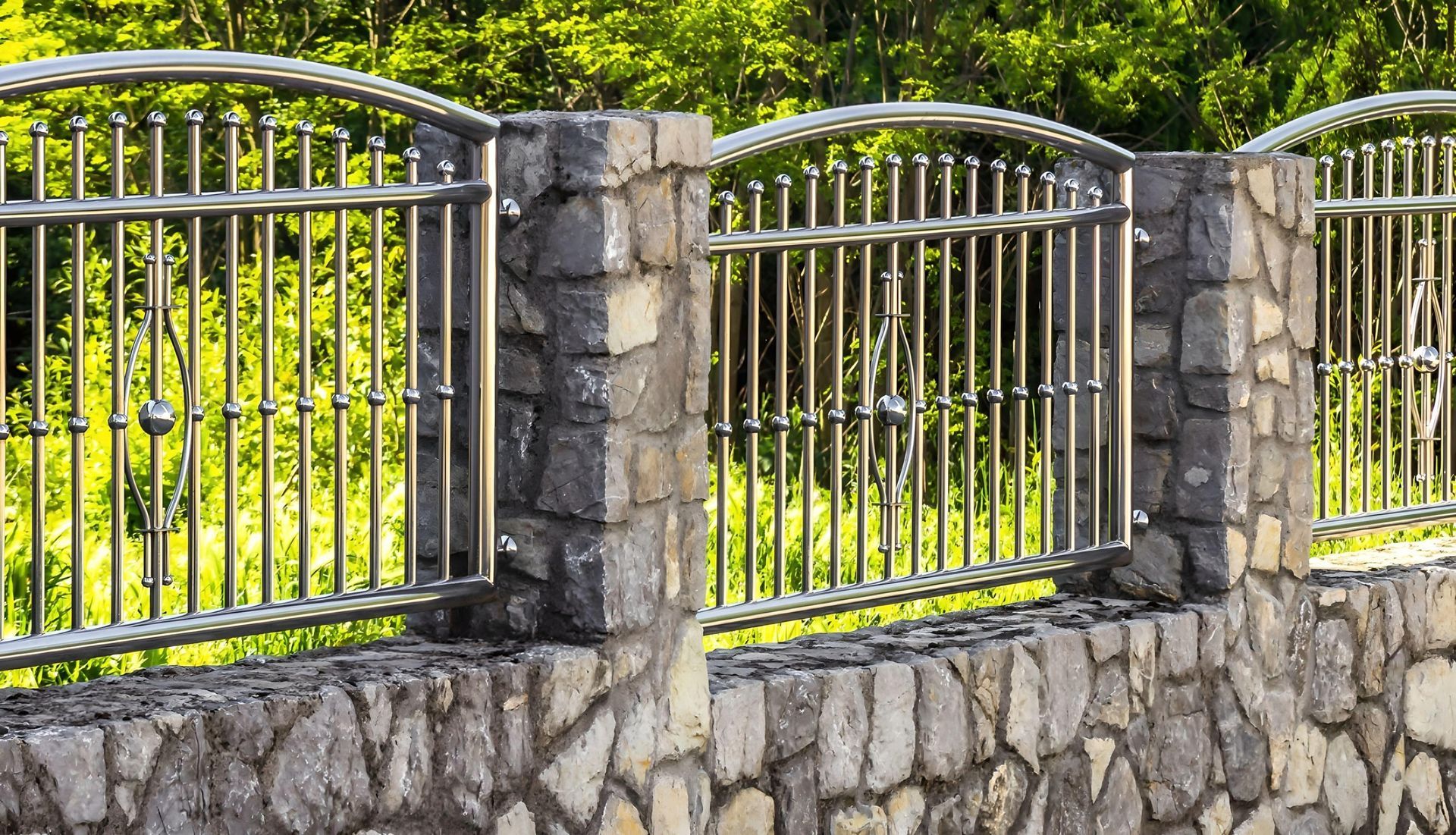 Stone wall with metal gates and stone pillars along a sunny garden fence