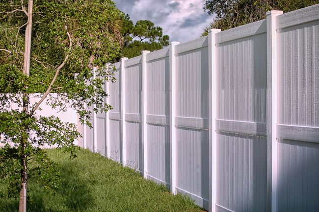 White privacy fence along a grassy yard with trees and a cloudy sky