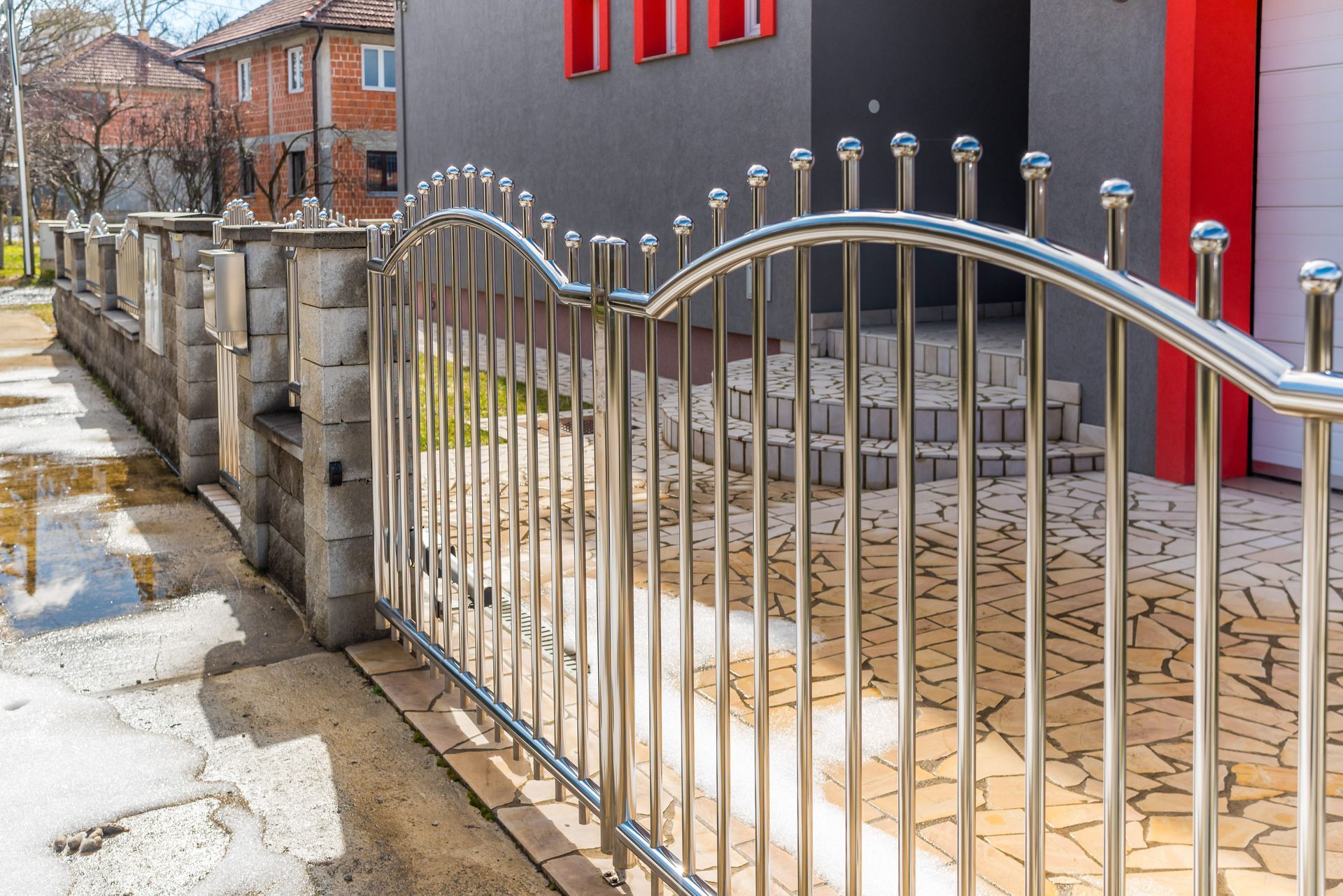 Silver metal gate beside a stone fence and modern house with red accents