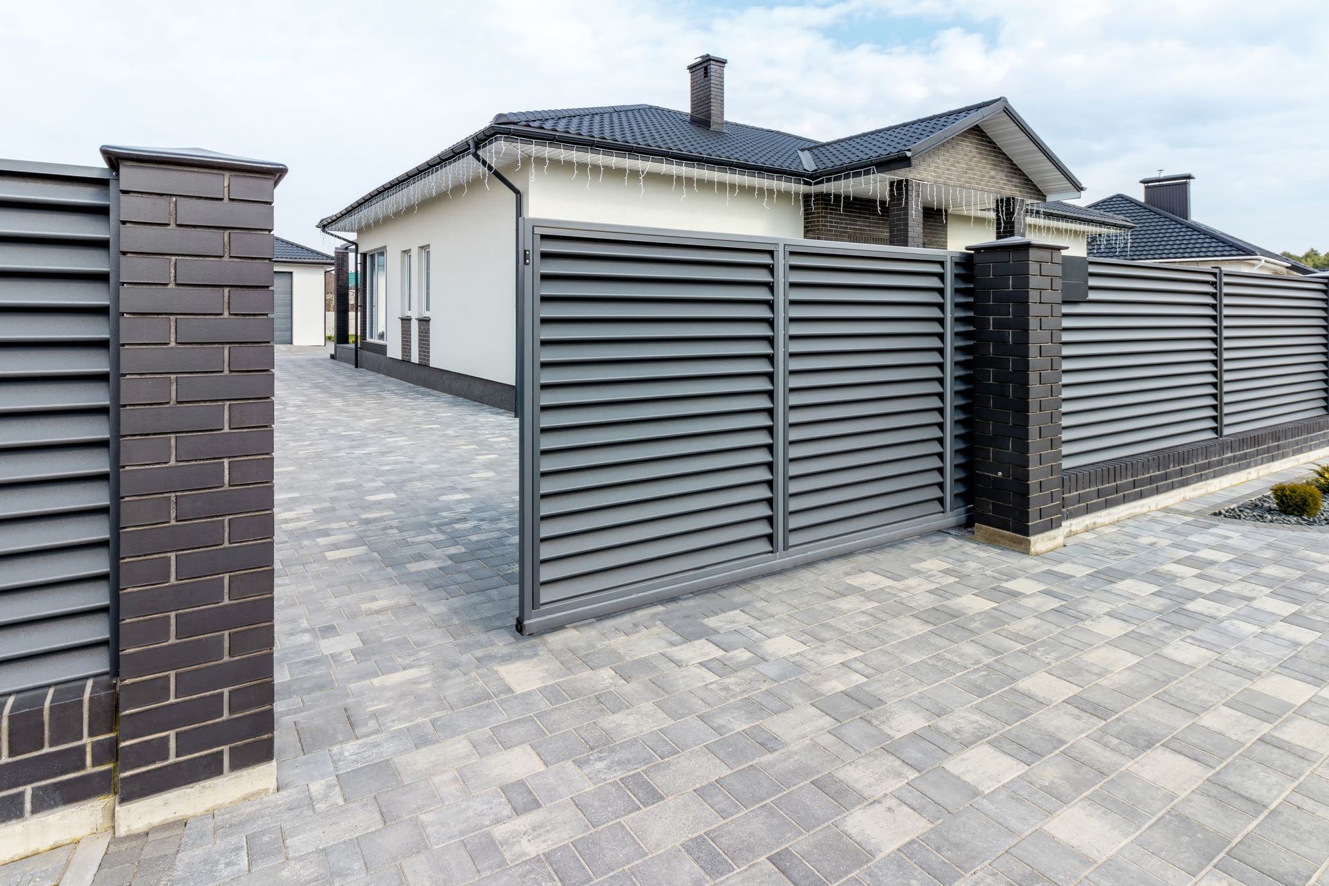Modern house entrance with gray metal gate, brick pillars, and paved driveway