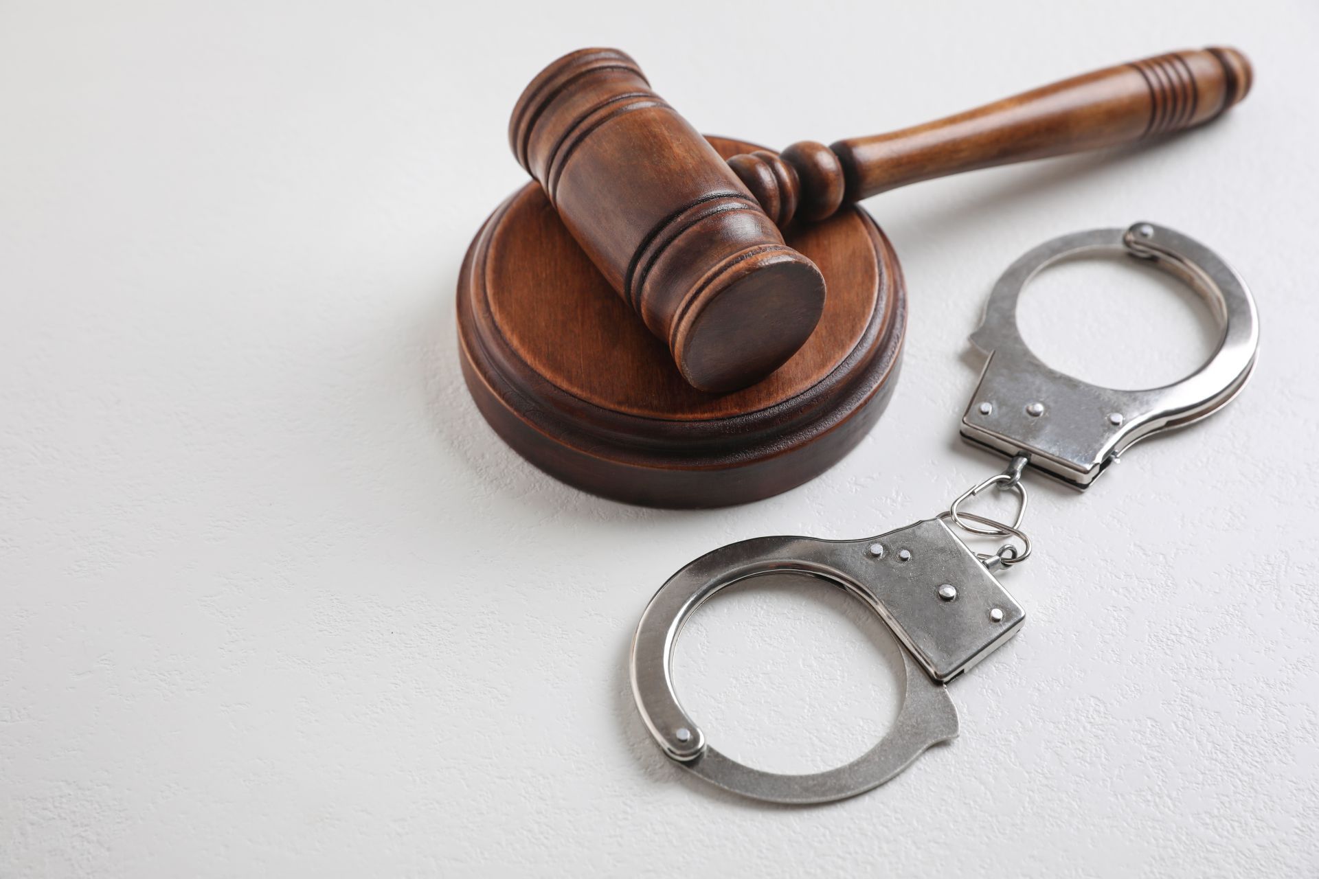 A wooden judge's gavel resting on a sounding block next to a pair of silver metal handcuffs on a white background.