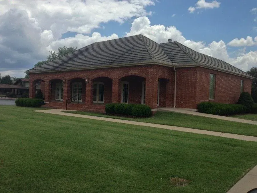 A large brick building with a gray roof is surrounded by lush green grass - Mountain Home, AR - Long Chiropractic
