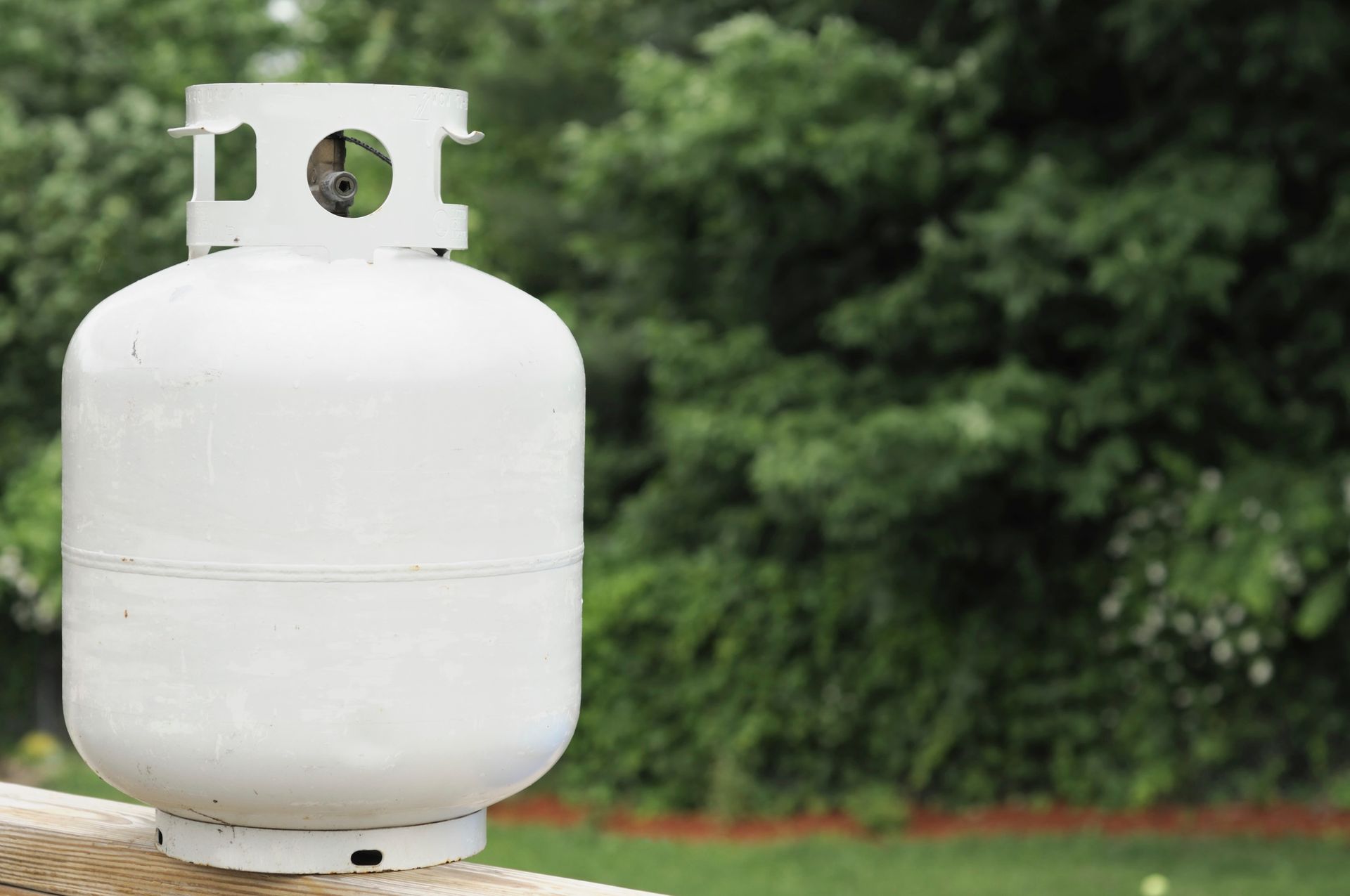 White propane tank with a yellow hose connected beside a house’s wooden exterior wall.