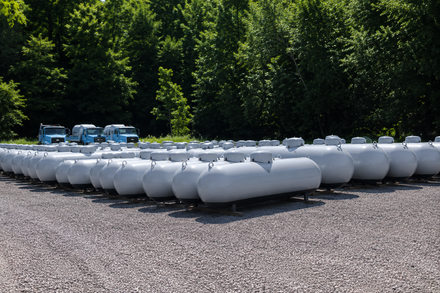 A white propane tank on a wood surface with a green foliage background in an outdoor setting A white propane tank on a wood surface with a green foliage background in an outdoor setting