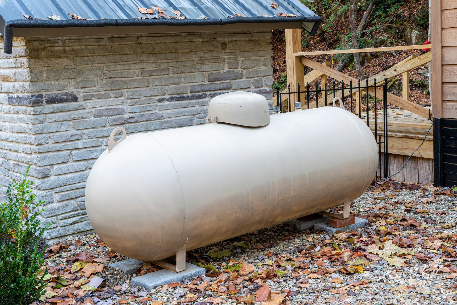 Large white propane tank standing on metal supports beside a wooden fence in a yard.