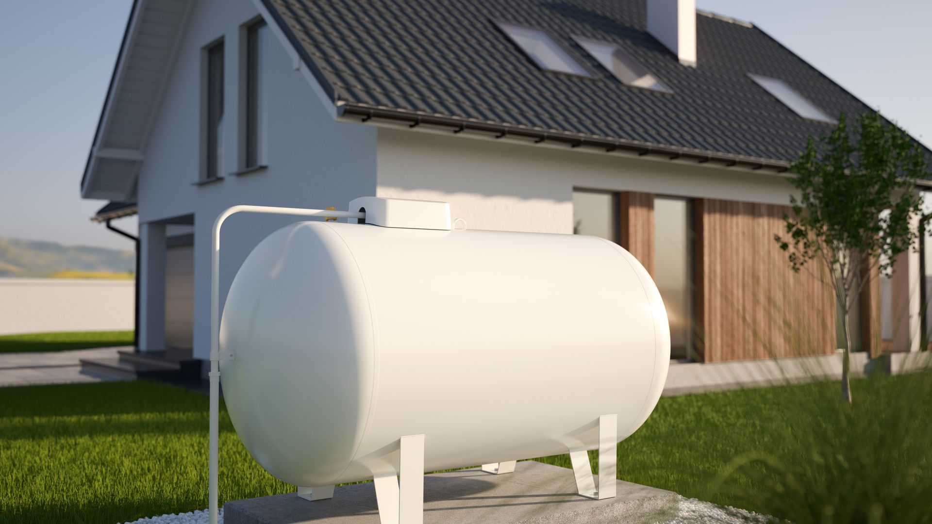 Large white propane tank standing on a grassy field with trees and homes in the background.