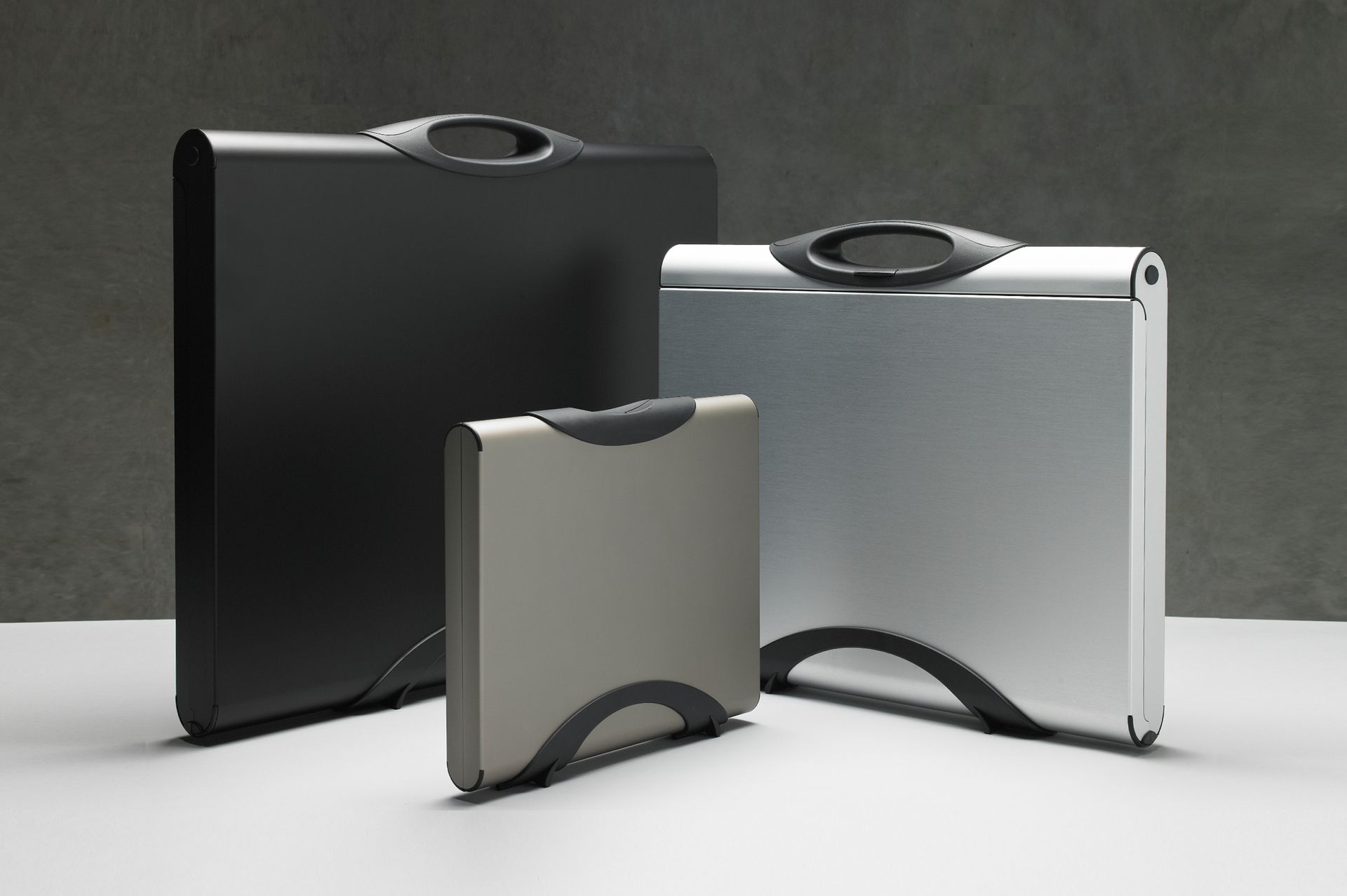 Three metallic briefcases of varying sizes with curved handles on a white surface.