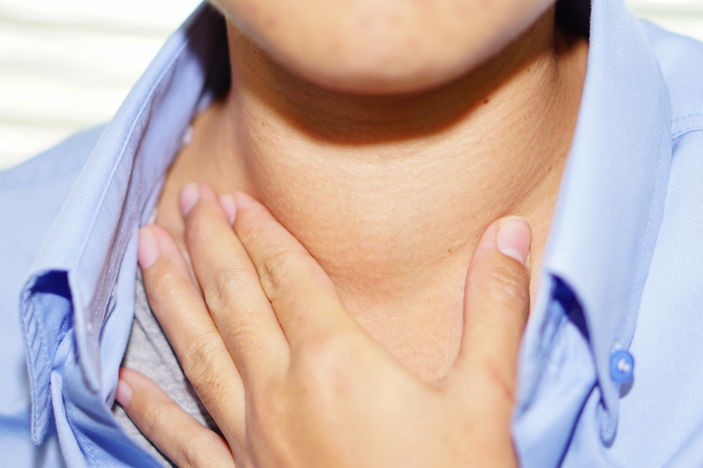 Person touching their swollen neck, likely indicating a health issue, in a blue shirt.